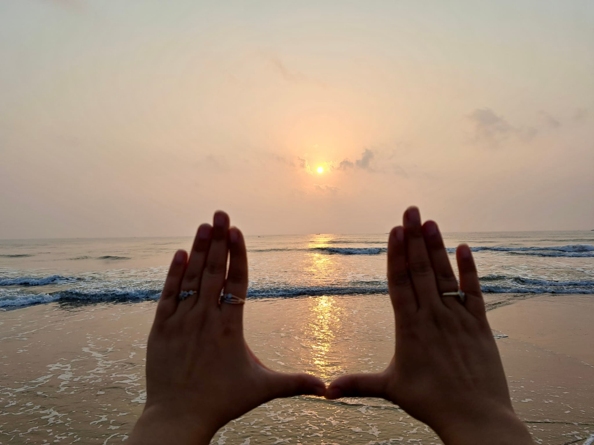 Two hands framing a sunrise over the ocean